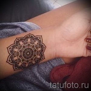 Фотография татуировки мандалы на запястье женщины. Рисунок выполнен в коричневых тонах.