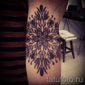 Фото тату мандалы на локте, выполненной в чёрно-серых тонах с добавлением растительных элементов. Рисунок татуировки с детальной проработкой.