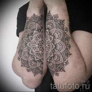Фотография двух симметричных татуировок мандал на локтях. Рисунки выполнены в черно-белом стиле с высокой детализацией и геометрическим узором.