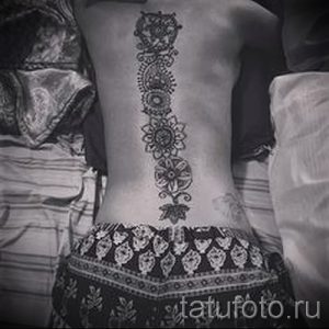 Фото тату: вертикальная полоса из мандал на спине девушки. Детализированный рисунок татуировки с геометрическими узорами и цветочными мотивами.