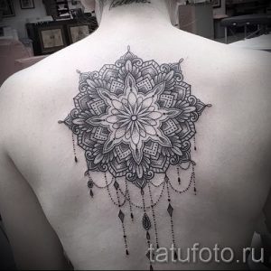 Фото тату мандалы на спине, украшенной подвесками. Детализированный рисунок татуировки с тонкими линиями и узорами.