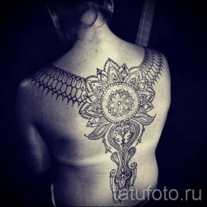 Фото тату мандалы на спине, выполненной в черном цвете. Деликатный рисунок татуировки с тонкими линиями и узорами.