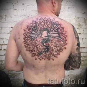 Фото тату мандалы с изображением дракона в центре, выполненной на спине мужчины. Детализированный рисунок татуировки с геометрическими узорами и тонкими линиями.