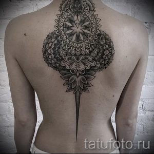 Фото тату на спине: мандала, в центре которой изображен цветок лотоса. Детализированный рисунок татуировки в черных тонах.