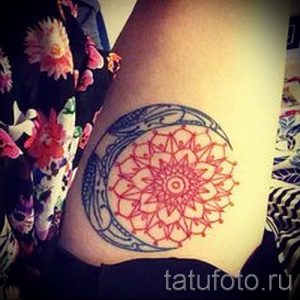 Красочное фото татуировки на боку, изображающей полумесяц с мандалой внутри. Рисунок выполнен в ярких красных и синих тонах.