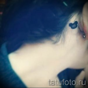 Фото тату на виске с изображением минималистичного силуэта головы Микки Мауса. Черно-белый рисунок татуировки небольшого размера.