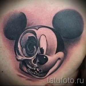Фото тату на плече с изображением черепа Микки Мауса. Черно-белый рисунок татуировки с реалистичными тенями и высокой детализацией.