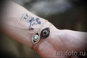 Фото тату Микки Мауса на запястье, рядом с золотыми браслетами. Небольшой рисунок татуировки в мультяшном стиле.
