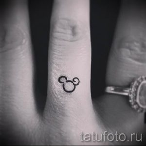 Фото минималистичной татуировки, изображающей только уши Микки Мауса на пальце. Рисунок выполнен в черном цвете.