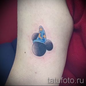 Фото миниатюрной татуировки Микки Мауса в образе волшебника с синей шляпой и звездами. Рисунок выполнен в ярких цветах.