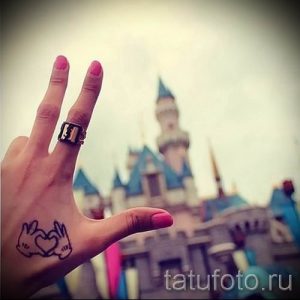 Фото тату: рука с татуировкой в виде двух рук Микки Мауса, образующих сердце. Рисунок татуировки на руке, на фоне замка.