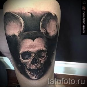 Черно-белая татуировка на руке с изображением черепа Микки Мауса. Реалистичный стиль, детальная проработка, мрачная атмосфера.