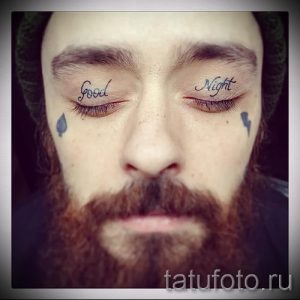 Фото тату над глазами мужчины с надписью "Good Night" на одном веке и "Night" на другом. Необычный рисунок татуировки, выполненный черными чернилами.