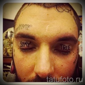 Фото тату: надписи "Stay" и "True" под глазами мужчины. Черно-белая татуировка, выполненная в минималистичном стиле.