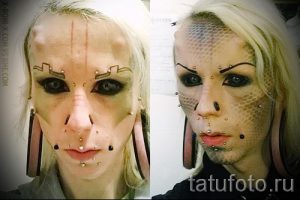 Фотография девушки с экстремальными модификациями лица, включая татуировки, пирсинг и растяжки в ушах. Изображение демонстрирует радикальный стиль самовыражения.