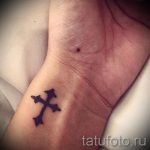 Фото тату: маленький черный крест на запястье. Классический и минималистичный рисунок татуировки, символизирующий веру.