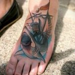 Фото тату с изображением старинного корабля и акулы, выплывающей из-под воды. Стиль рисунка - смесь традиционной морской татуировки и реализма.