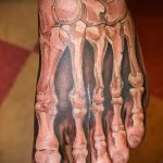 Фото тату скелета стопы с темными тенями. Реалистичный и детализированный рисунок, выполненный в черно-серых тонах. Идеально для любителей анатомии и мрачных татуировок.