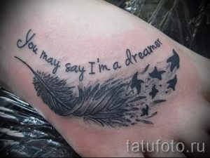 Фото тату на стопе: черное перо с летящими птичками и надписью 'You may say I'm a dreamer'. Изящный рисунок татуировки для вдохновения.