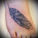 Фото тату на стопе: черное перо с замысловатыми узорами и цветочными элементами. Оригинальный рисунок татуировки в стиле орнамент.
