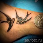 Фото татуировки на запястье с изображением двух летящих ласточек, выполненных в реалистичном стиле.