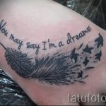 Фото тату с надписью "You may say I'm a dreamer" и изображением пера и летящих птиц на стопе. Выполнено в черно-белой гамме.
