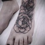 Фото тату пиона на стопе, выполненное в технике blackwork. Черно-белый рисунок с детально проработанными лепестками и листьями.