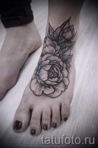 Фото тату пиона на стопе, выполненное в технике blackwork. Черно-белый рисунок с детально проработанными лепестками и листьями.