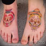 Фото тату двух черепов в стиле Day of the Dead на стопах. Красочный рисунок татуировки с цветами и традиционными элементами.