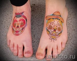 Фото тату двух черепов в стиле Day of the Dead на стопах. Красочный рисунок татуировки с цветами и традиционными элементами.