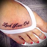 Фотография татуировки на стопе с надписью 'Luck Runs Out', выполненной красными чернилами в стилизованном шрифте.