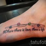 Фото тату надписи 'Where there is love, there is life' на женской стопе. Надпись украшена небольшими цветными звездочками.