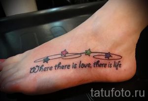 Фото тату надписи 'Where there is love, there is life' на женской стопе. Надпись украшена небольшими цветными звездочками.