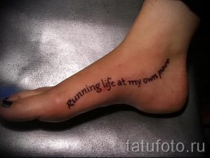 Фото тату на стопе: надпись 'Running life at my own pace' выполненная черным шрифтом. Мотивационная татуировка для активных людей.