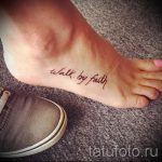 Фото тату надписи 'walk by faith' на стопе. Коричневый цвет, каллиграфический шрифт, религиозный стиль. Подходит для верующих людей.
