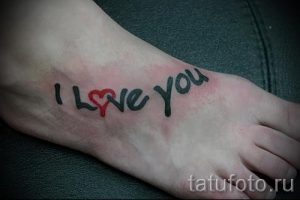 Фото тату надписи 'I Love You' с красным сердцем вместо буквы 'O' на стопе. Черный контур, яркий акцент, романтичный стиль. Идеально для пар.