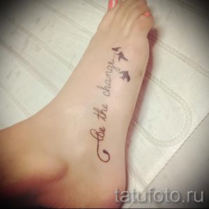 Фотография татуировки на стопе с надписью 'Be the change...' и изображением трех летящих птиц, выполненных черными чернилами.