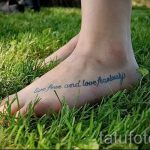 Фото тату надписи 'Live free and love fearlessly' на женской стопе. Надпись выполнена голубым цветом, на фоне зеленой травы.