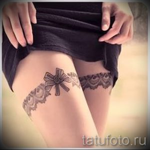 Фото тату подвязки с бантом на бедрах, выполненной в черно-белой гамме. Детализированный рисунок татуировки с акцентом на кружевные элементы.