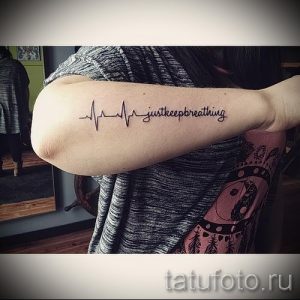 Фото тату: Черная татуировка пульса, переходящего в надпись 'just keep breathing' на руке. Мотивирующий и вдохновляющий дизайн.