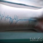 Фото тату на запястье: тонкая синяя линия электрокардиограммы, изящно обвивающая руку. Минималистичный рисунок татуировки.