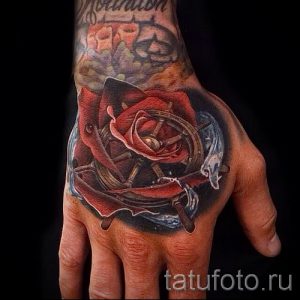 Яркая татуировка на руке, изображающая красную розу, компас и игральные карты. Детализированный рисунок татуировки в цвете.