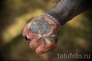 Минималистичная татуировка на руке, изображающая черную розу с листьями. Простой и элегантный рисунок татуировки.
