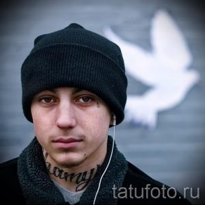 Фото тату: мужчина с татуировками на лице, включая слезы под глазами и надпись на щеке. Рисунки выполнены черными чернилами.