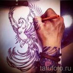 Фото эскиза татуировки феникса, нарисованного на руке. Детализированный рисунок татуировки с расправленными крыльями.