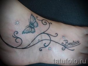 Фото татуировки на лодыжке с изображением серой бабочки, имени 'Beatrice' и маленьких звездочек. Нежный и персонализированный рисунок татуировки.