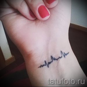 Фото тату: маленькая, черная татуировка в виде линии кардиограммы на запястье девушки.