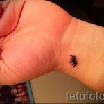 Фотография женского запястья с маленькой татуировкой в виде черной короны, выполненной в минималистичном стиле.