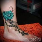 Фото тату на лодыжке: яркая бирюзовая роза, обвитая четками с крестом, выполненная в реалистичном стиле.