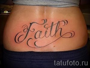 Фото тату: Черно-белая татуировка надписью 'Faith' на пояснице, выполненная каллиграфическим шрифтом.